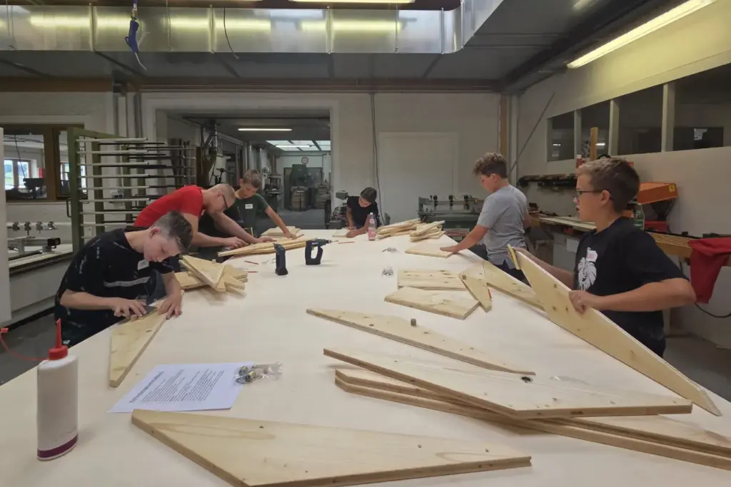 Kinder stehen rund um einen Tisch und schleifen Holzteile